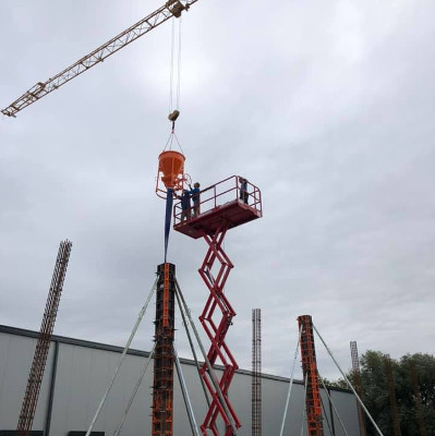 Arbeiter auf einer mobilen Plattform montieren Bauteile mit einem Kran an einer Baustelle.
